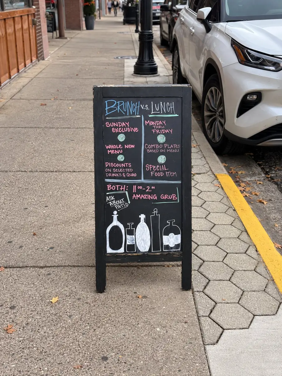 A chalk sandwich board on a sidewalk comparing Brunch and Lunch: Sunday exclusive, whole new menu, Monday through Friday combo plates, both 11 to 2.
