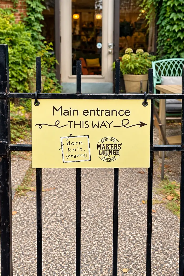 A yellow sign on an iron gate pointing to the main entrance of darn. knit. anyway and its Makers Lounge.